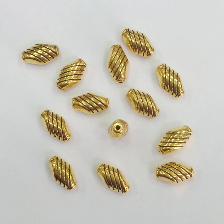 <p>Металлическая бусина в форме вытянутого ромбика с насечками. Цвет золотой с чернением. Оттенок может отличаться от фотографии. На покрытии возможны пятнышки. Диаметр отверстия около 1 мм. Цена за 10 грамм (около 13 бусин, фасуются без проверки на дефекты).</p>